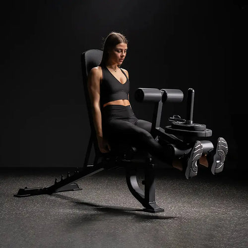 Frau in Sportkleidung sitzt auf einer Beinstreckmaschine im Fitnessstudio und streckt die Beine nach vorne