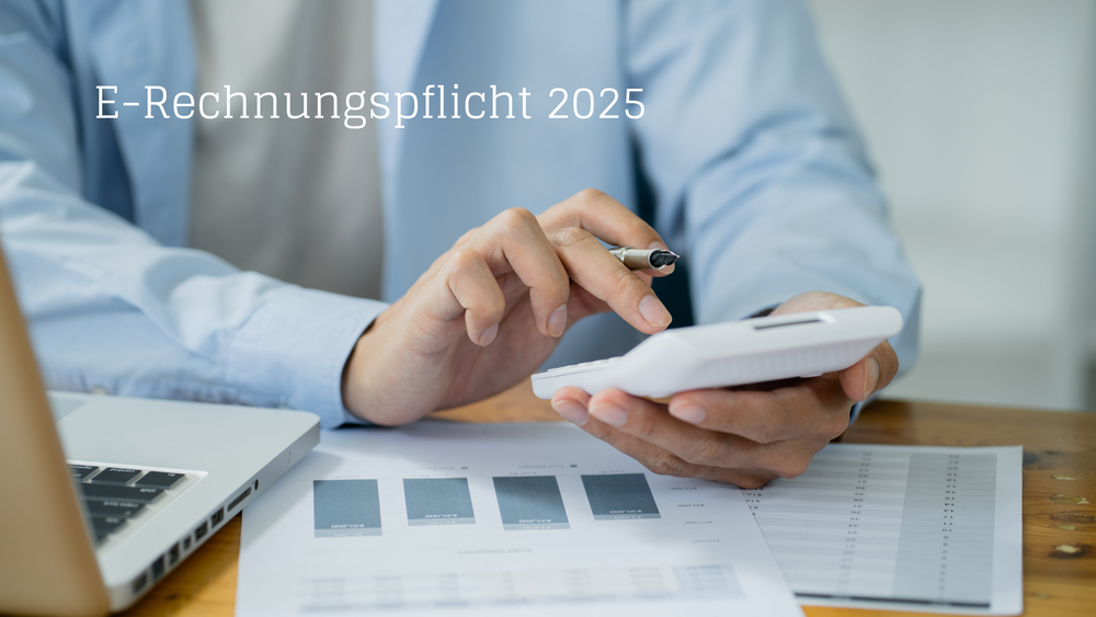 Hand einer Person mit Hemd, die einen Taschenrechner bedient, auf einem Schreibtisch mit Laptop und Dokumenten, Text 'E-Rechnungspflicht 2025'