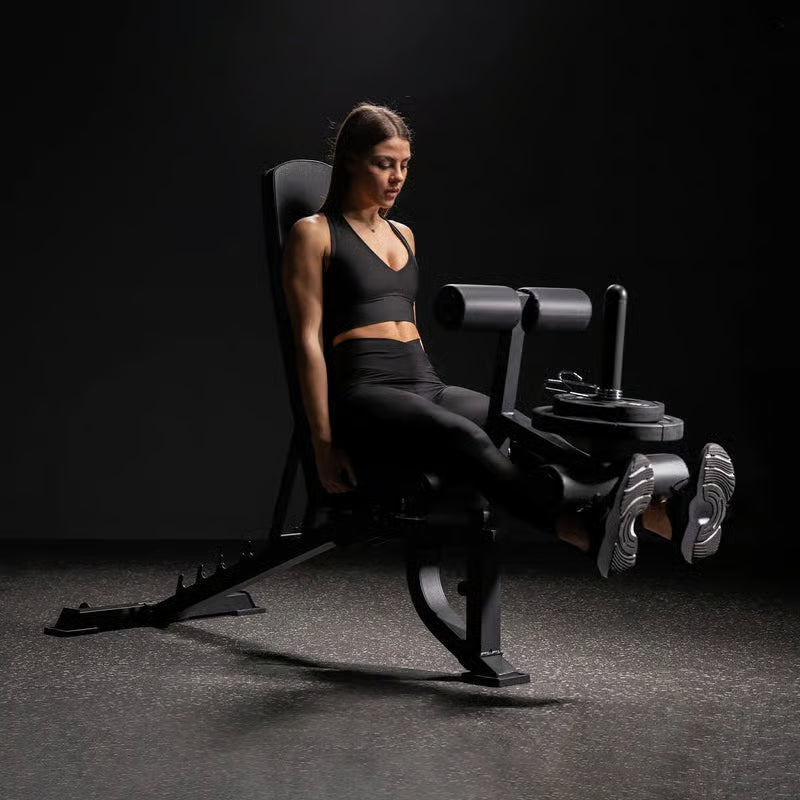 Frau in Sportkleidung sitzt auf einer Beinstreckmaschine im Fitnessstudio und streckt die Beine nach vorne